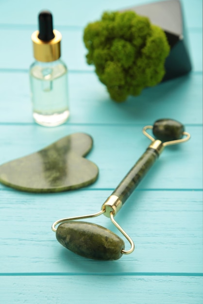 Rullo di giada verde e pietra di gua sha per massaggio facciale e su sfondo blu accessori per la bellezza della casa e per la cura di sé rullo per il viso per il trattamento delle rughe antietà vista dall'alto disteso