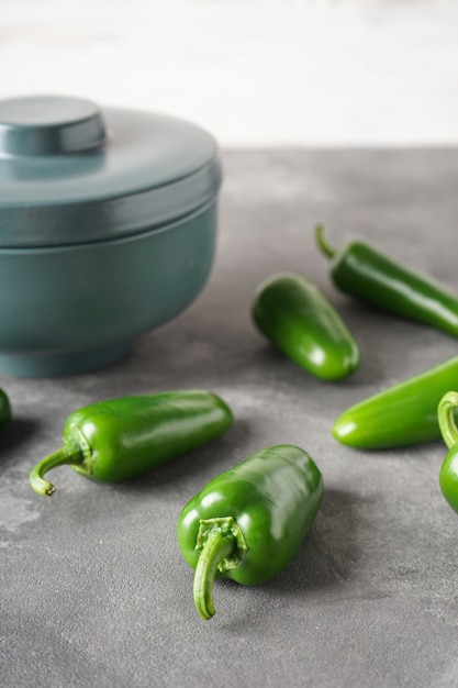 Green jalapeno peppers in a ceramic bowl on a gray background. Vertical.