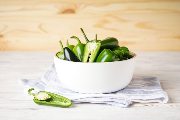 Green jalapeno peppers in a white wooden plate on a wooden background.