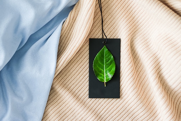 Green leaf on clothing tag and organic fabric background sustainable fashion and brand label concept