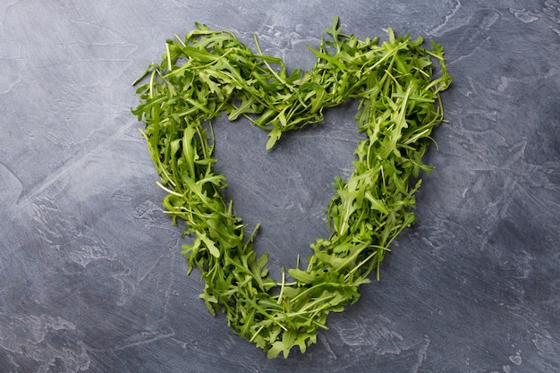 Foglie verdi di rucola disposte a forma di cuore su sfondo scuro.