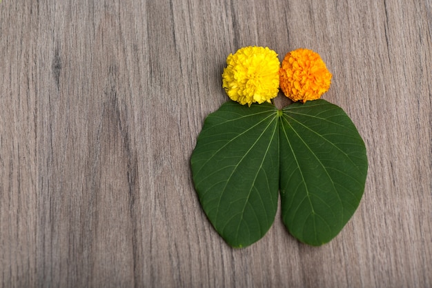 Green leaves and marigold flowers on a wooden background