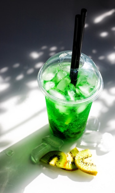 얼음과 키위 조각이 있는 녹색 레모네이드. 플라스틱 컵이 탁자 위에 있습니다.