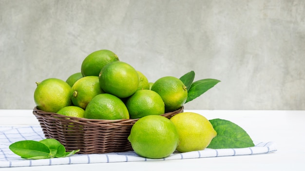 Green lime in a basket on a white wooden table.