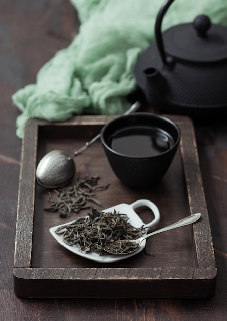 Tè verde sfuso con infusore a filtro vintage e teiera in ferro con tazza in scatola di legno con panno verde su fondo di legno