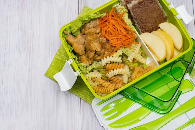 Photo green lunch box with cutlery pasta with chicken carrots cut apple and toast with chocolate paste healthy eating copy space