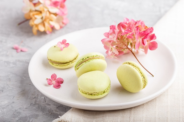 Green macarons or macaroons cakes on white ceramic plate on a gray concrete surface  side view, selective focus.