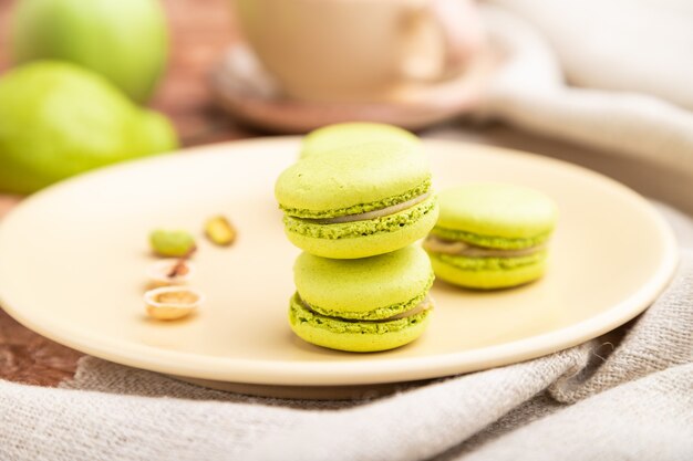 Green macarons or macaroons cakes with cup of coffee on a brown concrete surface and linen textile