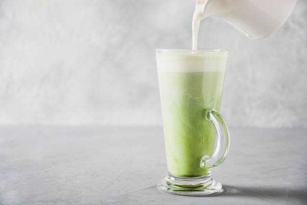 Green matcha tea and milk in latte glass on grey table. 