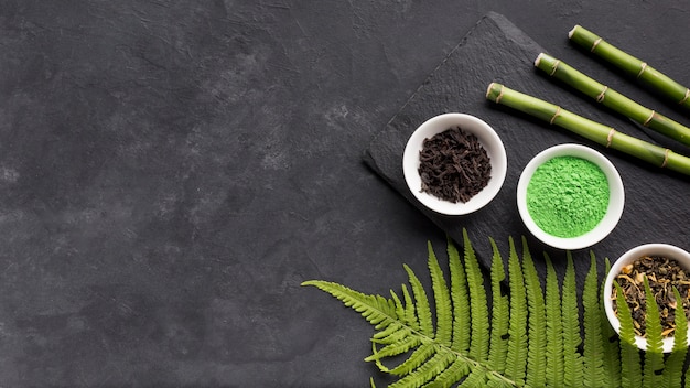 Photo green matcha tea powder and dry herb with bamboo stick on black textured surface