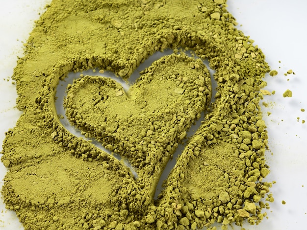 Photo green matcha tea powder on a white background with a heart shape. the concept of health.