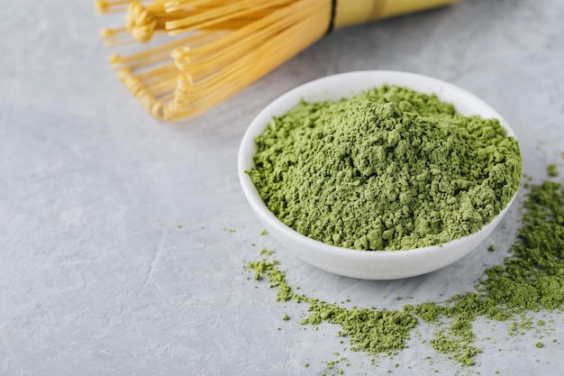 Green matcha tea powder in white bowl on gray stone background