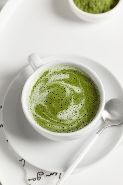 Green matcha tea with milk on cup with spoon on white table