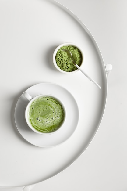 Green matcha tea with milk in cup with spoon on white table