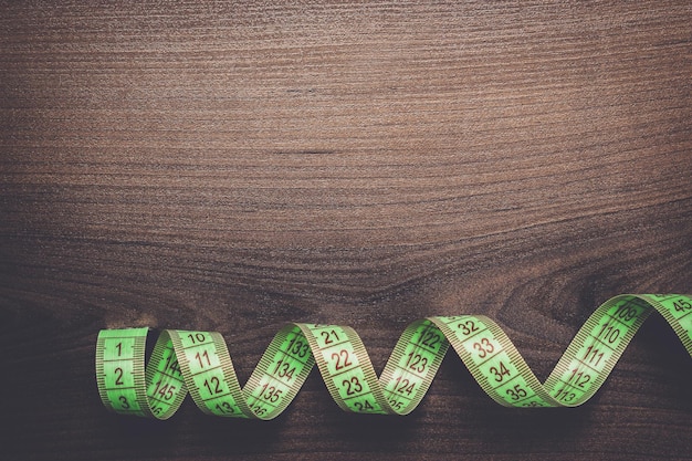 Green measuring tape over brown wooden background