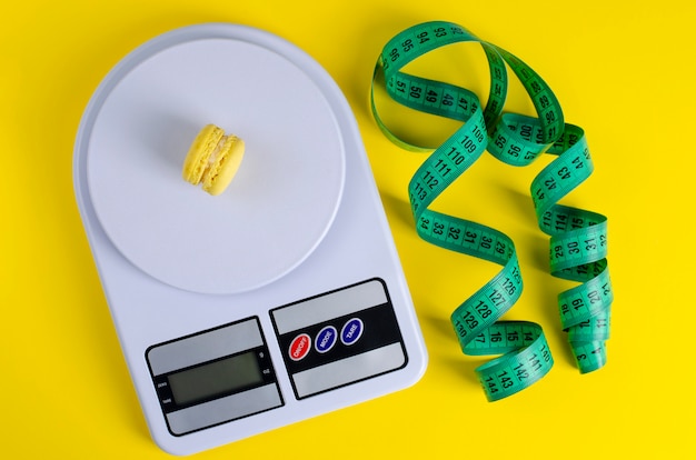 Green measuring tape, digital kitchen scales with macarons on yellow