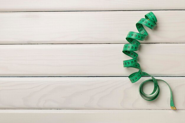 Green measuring tape on wooden background top view