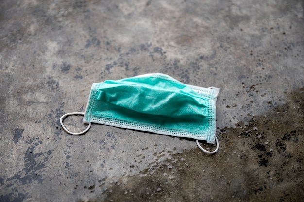 Green medical mask wet and discarded on cement floor in rainy