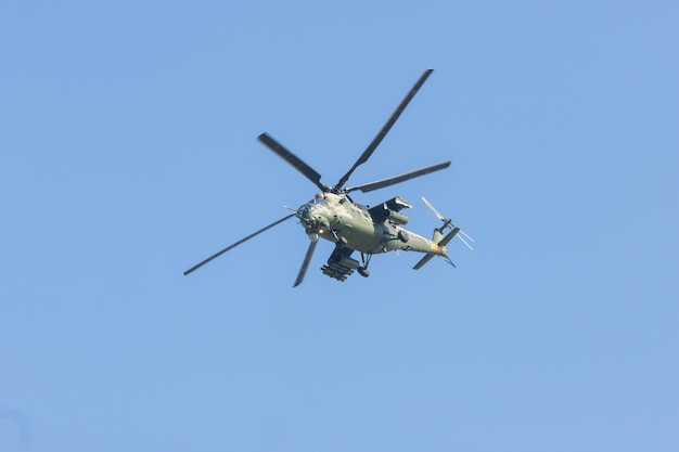 A green military helicopter flying up clear blue sky