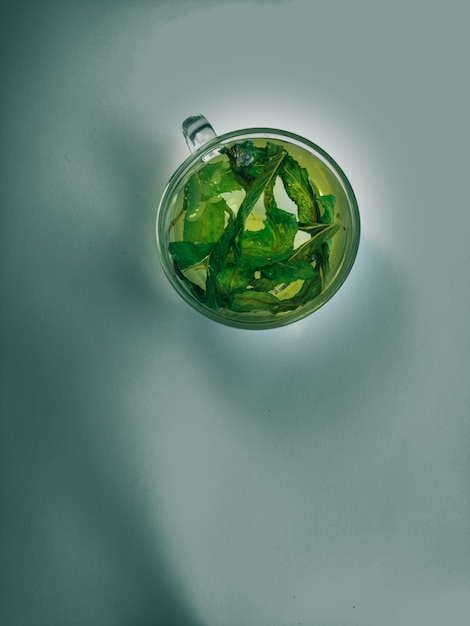 Tè alla menta verde in una tazza di vetro con foglie di menta su uno sfondo verde vista dall'alto