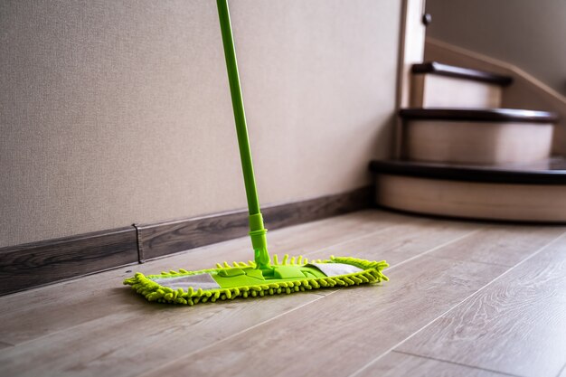 Photo green mop standing near white wall. cleaning gear. householding.