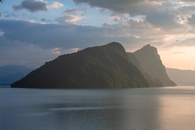 A green mountain standing by a lake during the sunset