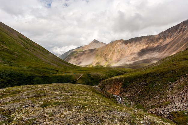 Green mountain valley with a small river in a crevice Clouds over the high mountains On the ground grass and moss Horizontal