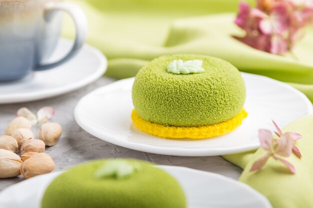 Green mousse cake with pistachio cream and a cup of coffee on a gray concrete surface. side view, selective focus.