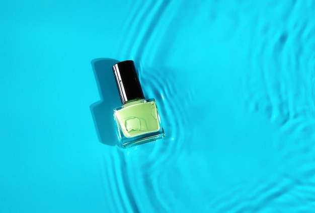 Green nail polish bottle in blue water top shot. nail polish\
bottle in clean water.