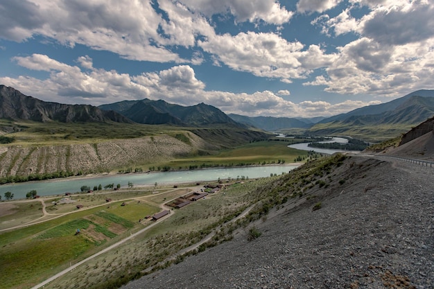 A green natural valley with the mountain beauties of the hillsides and a pond flowing in the distance. There are wooden animal pens on the river bank. Country territory for animals.