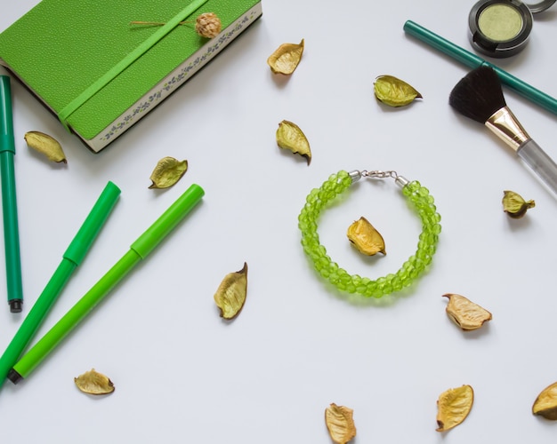 Green notebook and pens, cosmetics on white background