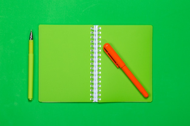 Green notebook and two pens on a color background