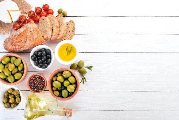 Foto olive verdi e olive nere pane all'olio formaggi e snack cucina italiana su un tavolo di legno bianco vista dall'alto spazio libero per il testo