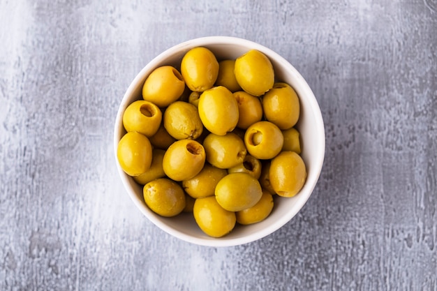 Green olives in a bowl on grey table. Top view