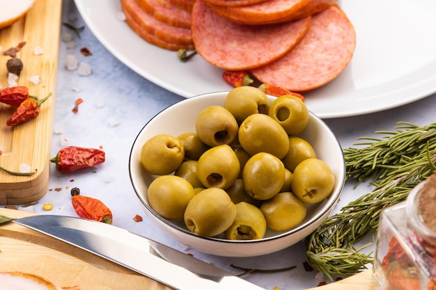 Photo green olives in a bowl on the table surrounded by products such as sausages bacon and spices
