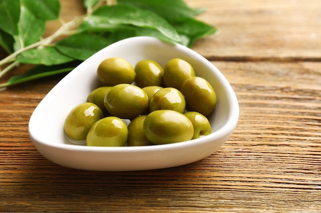 Green olives in bowl with leaves on table close-up