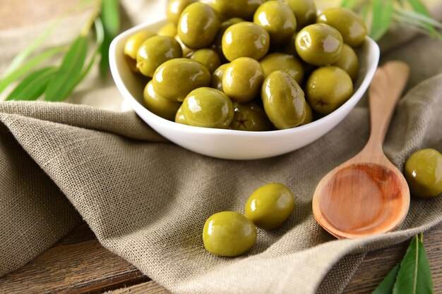green olives in bowl with leaves on table closeup