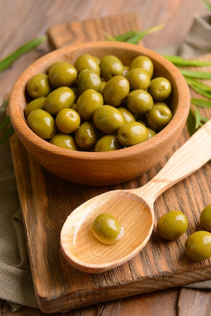 Green olives in bowl with leaves on table closeup
