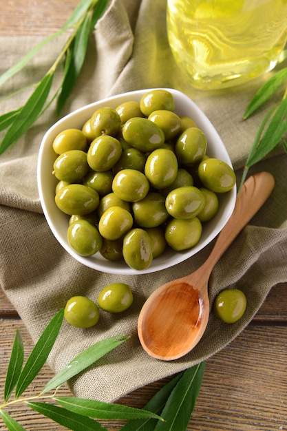 Green olives in bowl with leaves on table closeup