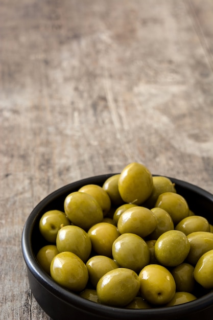 Green olives in bowl on wooden table copy space