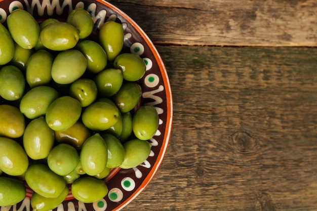 Green olives in brown bowl on wooden surface  