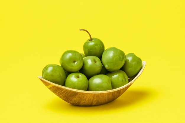 Green olives in eco friendly wooden bowl isolated on yellow background