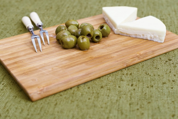 Green olives and goat cheese on a wooden board.