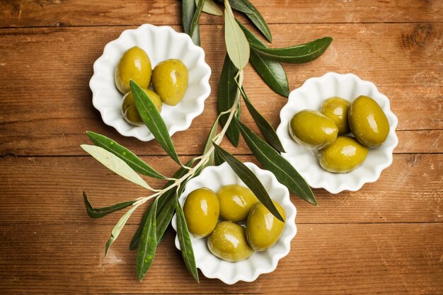 Green olives in white bowls on a wooden table in a top view