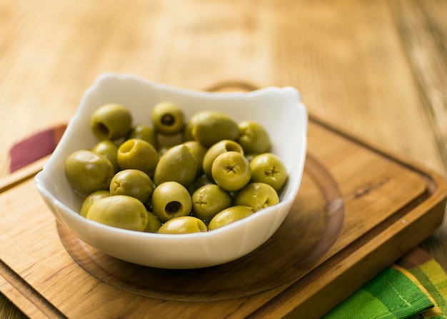 Green olives on a white plate on a wooden background
