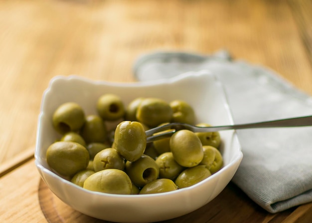 Green olives on a white plate on a wooden background