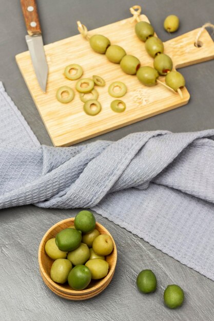 Green olives in a wooden bowl Gray napkin Knife and chopped olives on a cutting board