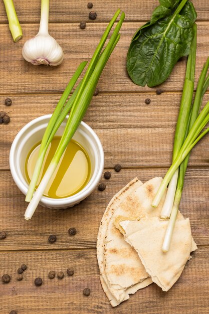 Green onions in bowl with olive oil. Pieces of pita, allspice and garlic on table. Wooden background. Top view