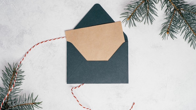 Green open Christmas envelope on white concrete background with blank kraft paper greeting card. Copy space. Top view