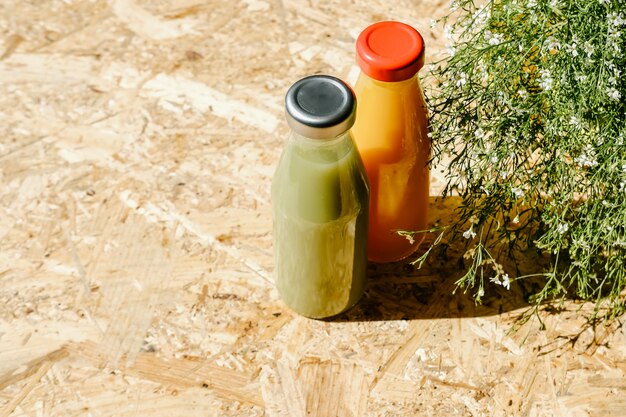 Green and orange detox juices next to bush